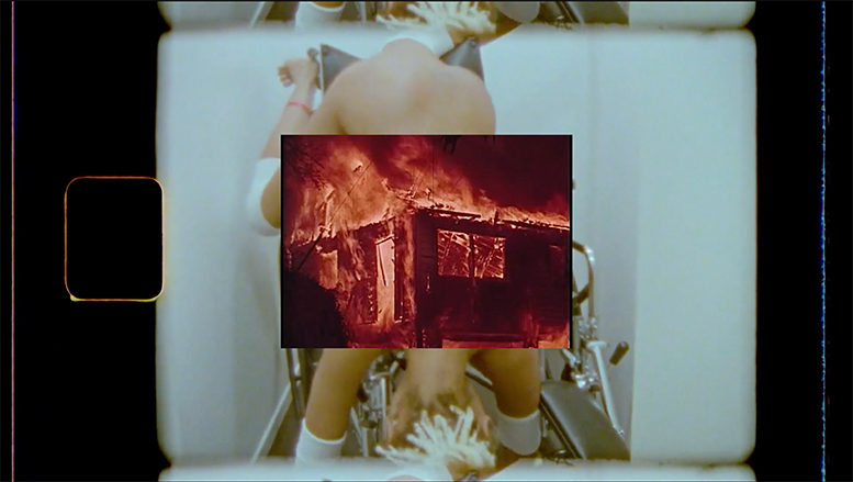 Building burning in foreground frame with woman mounting a wheelchair headfirst, naked except for knee, elbow, and wrist wraps. Building burning in foreground frame with woman mounting a wheelchair headfirst, naked except for knee, elbow, and wrist wraps.
