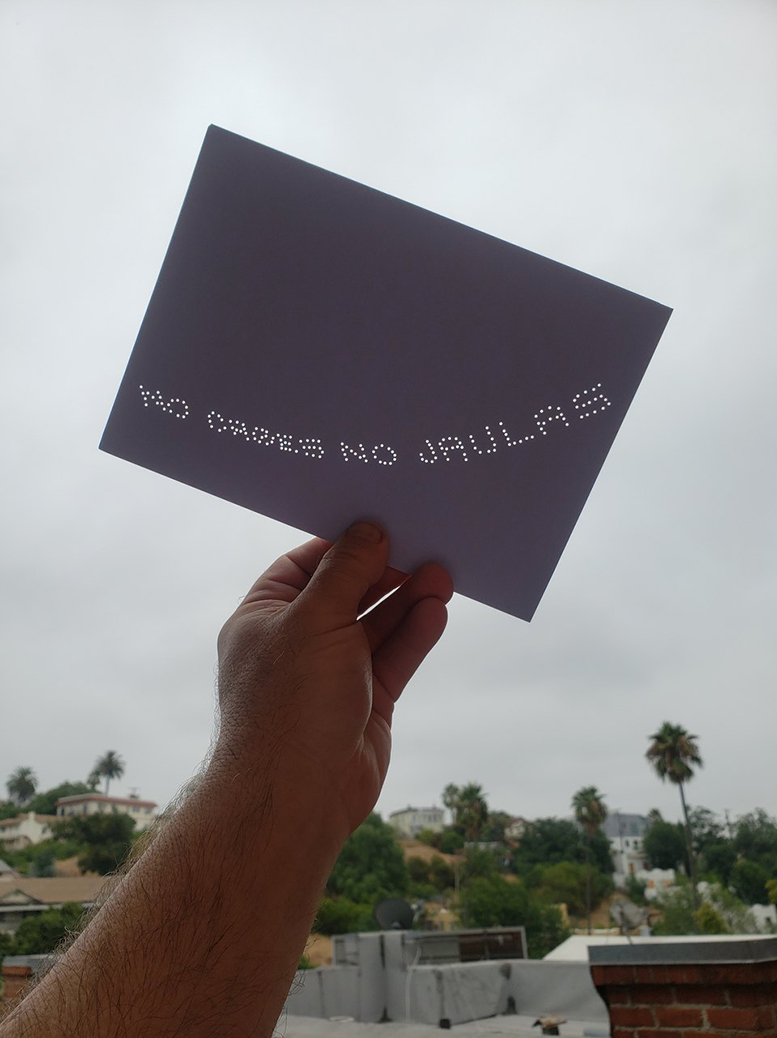 Hand holding postcard that reads “NO CAGES NO JAULAS” with LA in background image