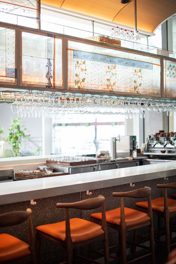 A bar with glass shelving above that shows off backlit cloth with patterns.