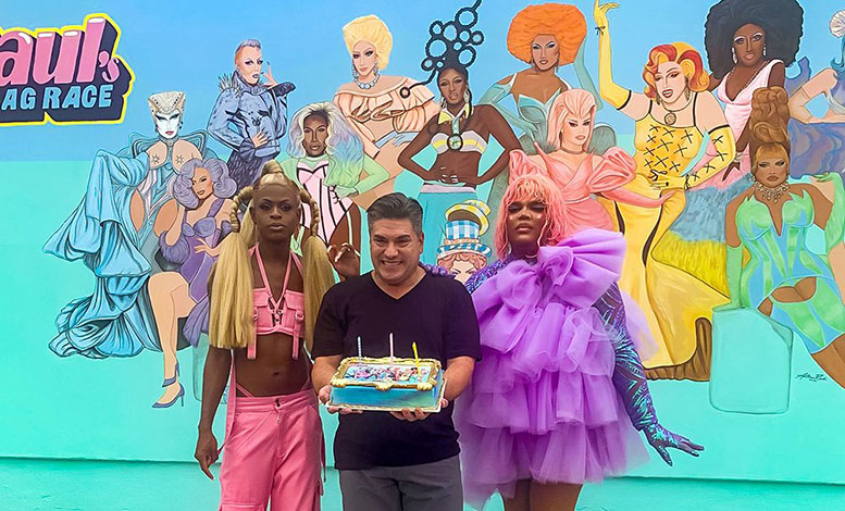 An artist poses with two people in drag in front of the mural he painted.