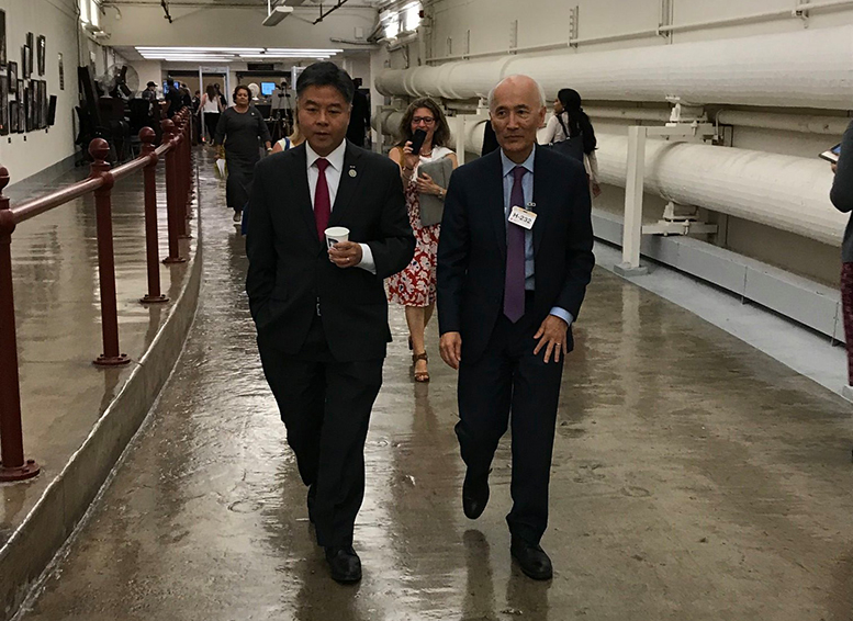 Roger Wakimoto and Congressman Ted Lieu are wearing suits and walking down a corridor.