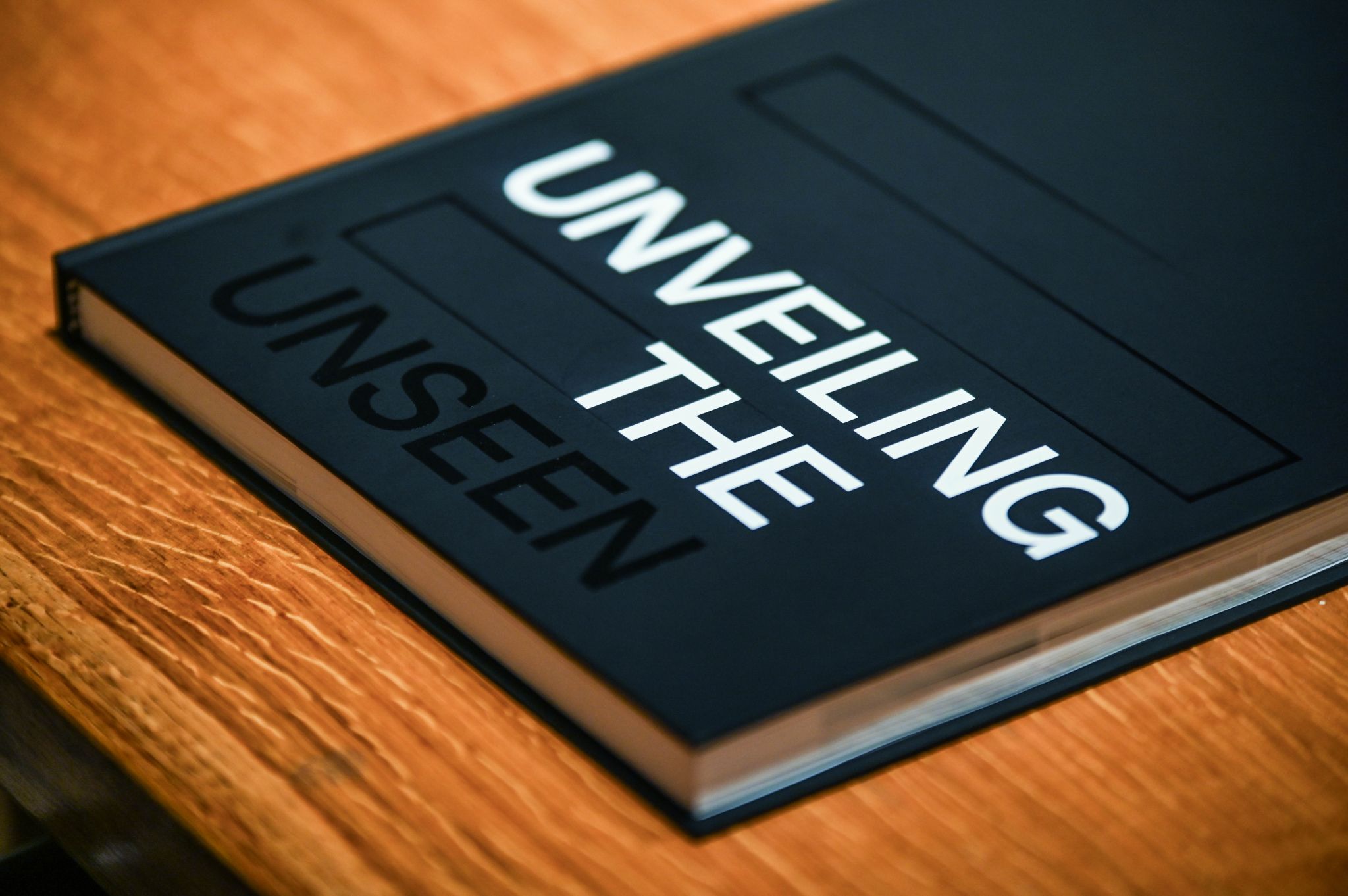 Black book titled &ldquo;Unveiling the Unseen&rdquo; resting on a wooden table.