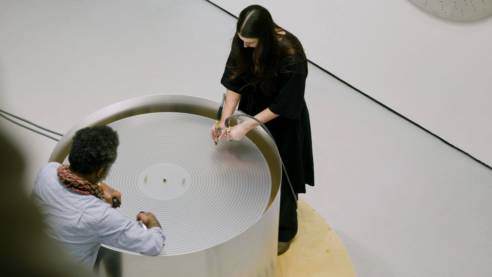 Two people stand around a large circular table with concentric grooves.