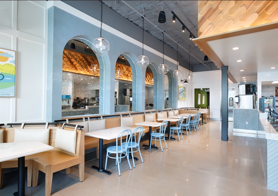 Bright, modern restaurant interior with blue arched wall accents, booth seating, light blue chairs, and globe pendant lights hanging above dining tables.