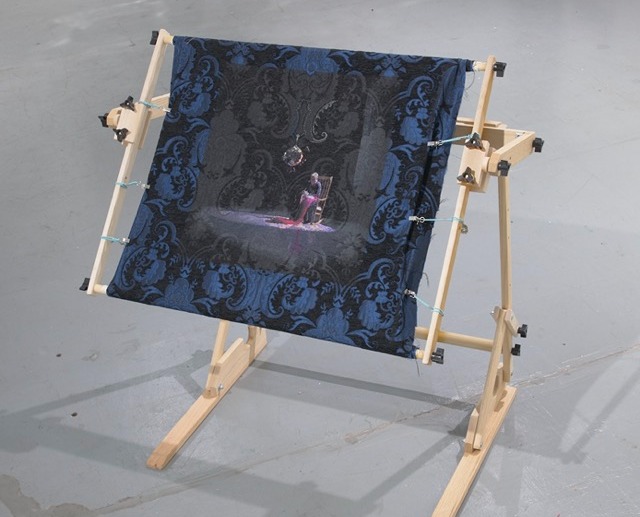 Installation view of Sharon Kagan's artistic work "Needles or Knvies?", a needle work piece depicting herself stretched on a canvas.